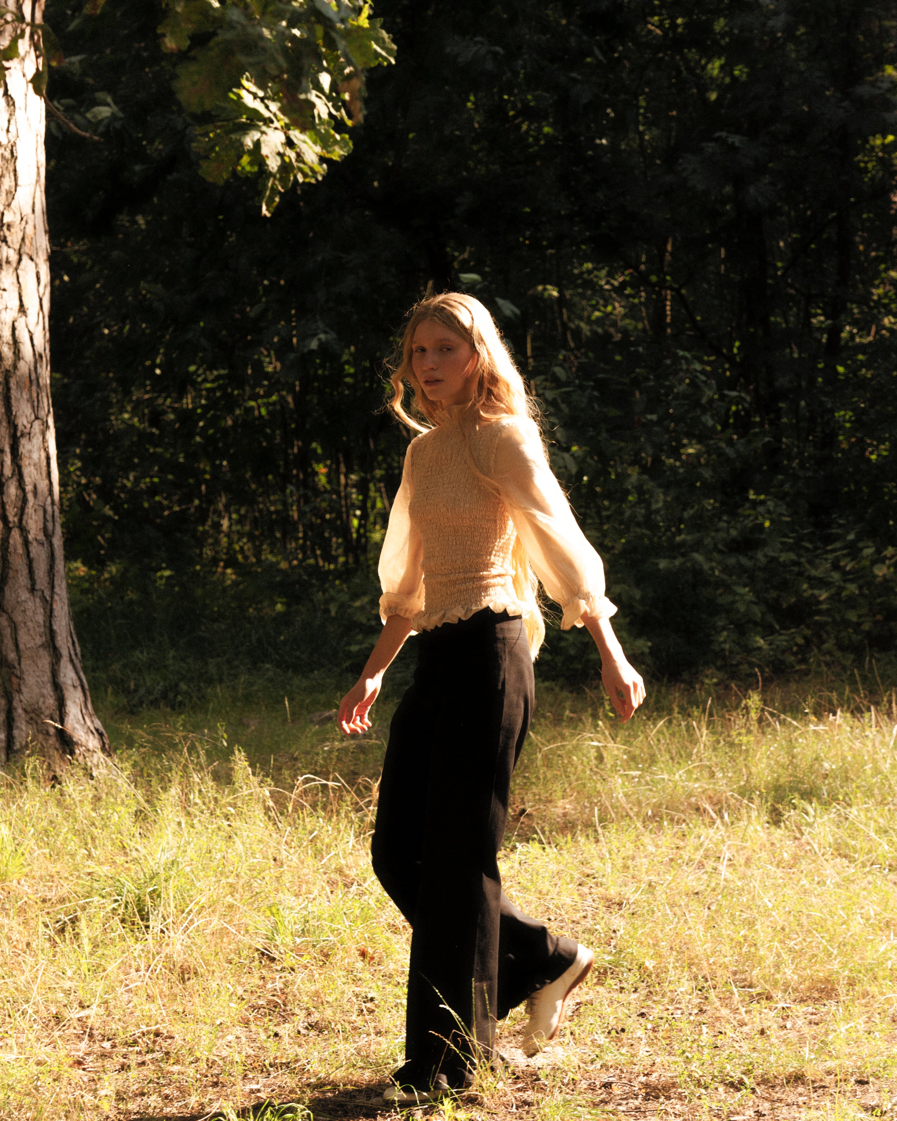 Woman in a beige blouse 3/4 sleeves walking in a field with trees