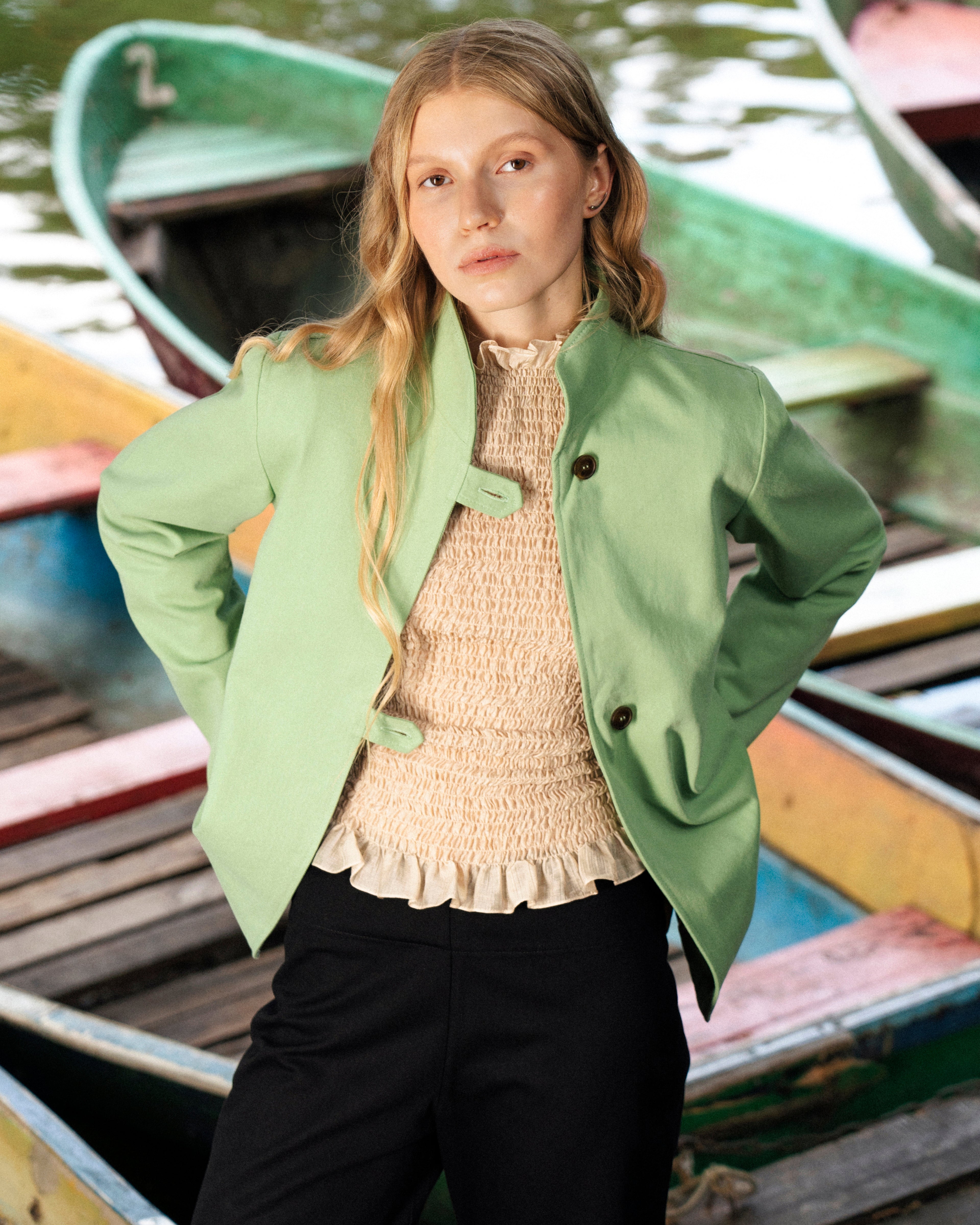 Woman in a green jacket standing among colorful boats on water