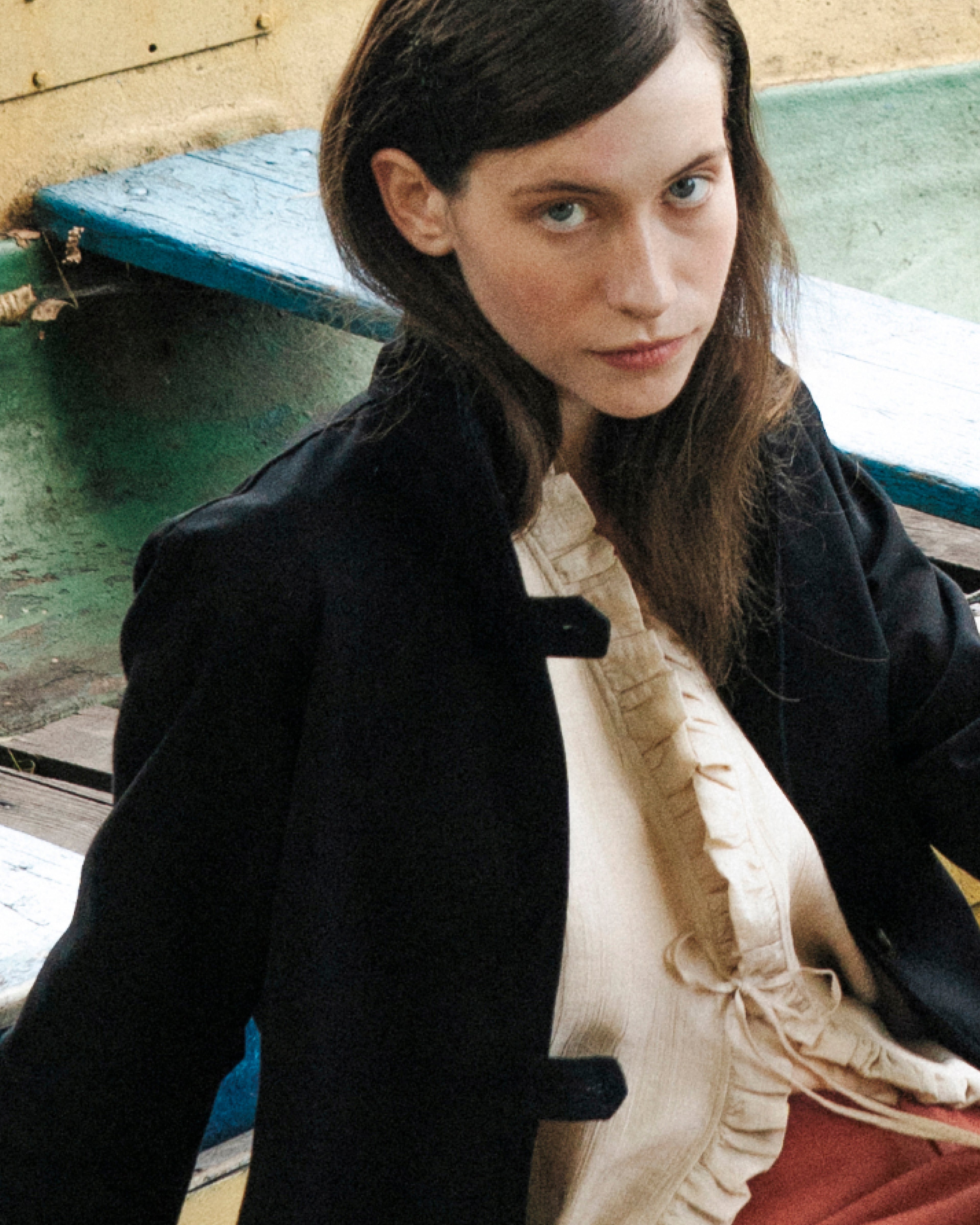 Woman wearing a black jacket and beige blouse sitting on a colorful wooden boat.