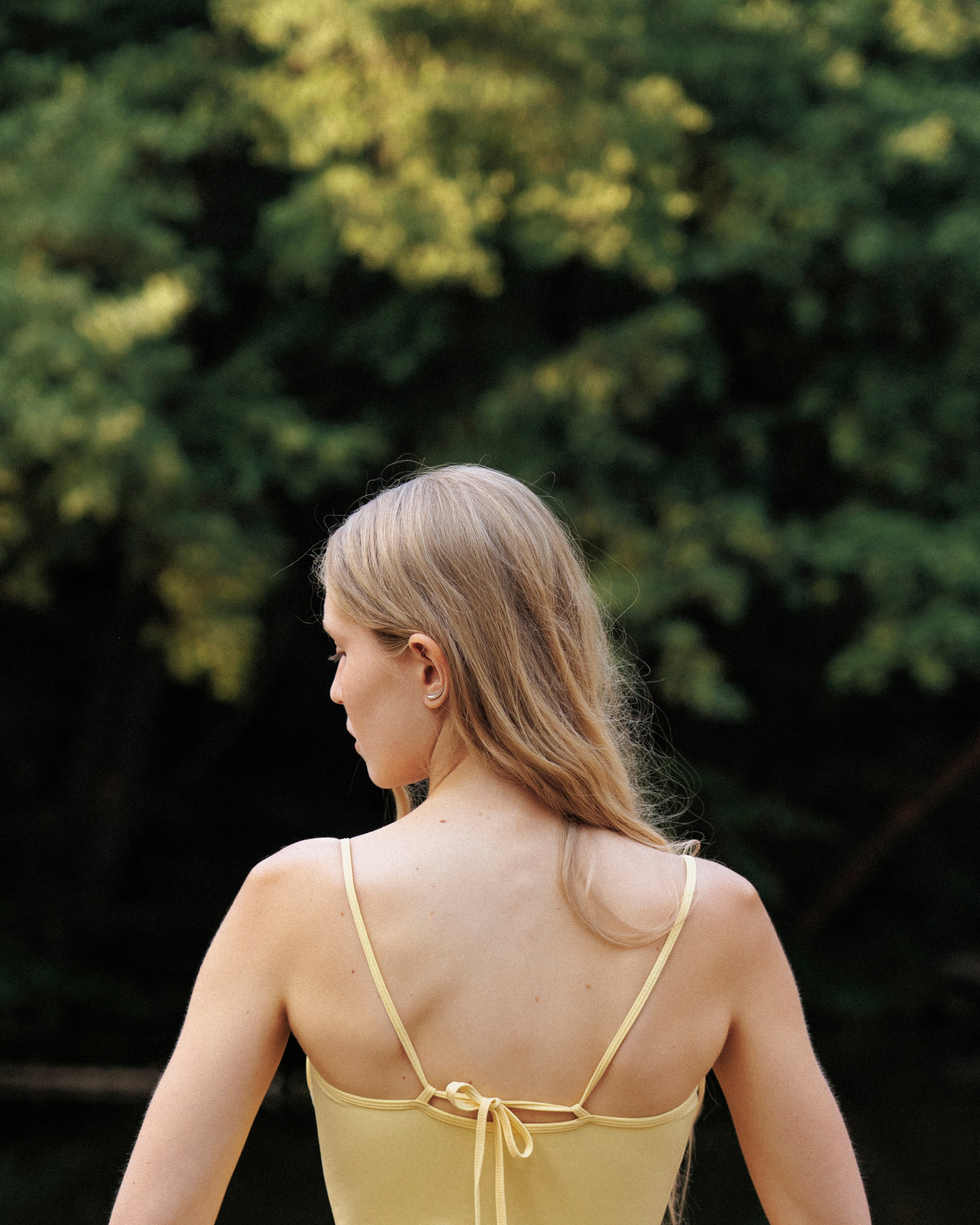 Woman wearing a yellow one-piece swimsuit with thin back strap against a blurred green background